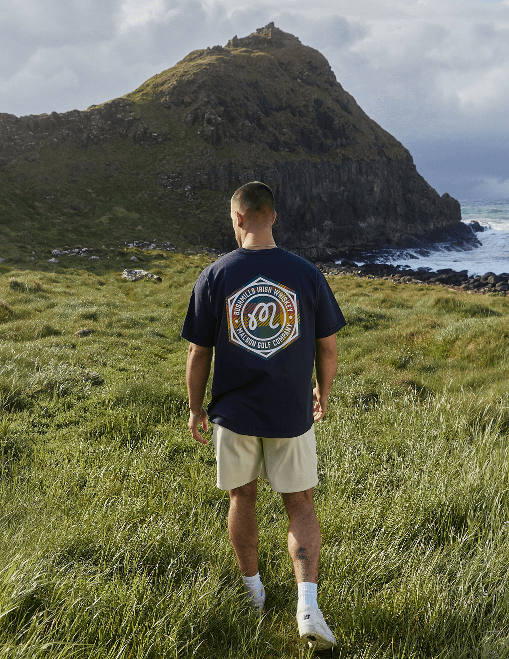 Back of Bushmills x Malbon navy tee on model overlooking Irish seas.