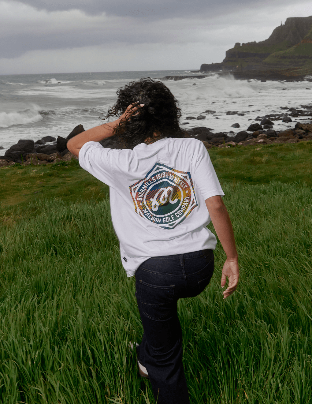 Back of Bushmills x Malbon white tee on model on a cliff by Irish seas.