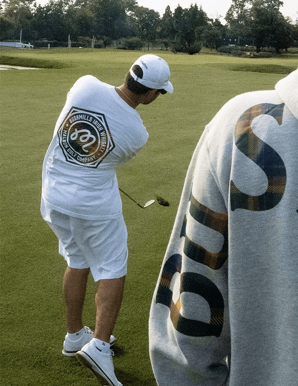 Man golfing wearing white Bushmills x Malbon collab tee.