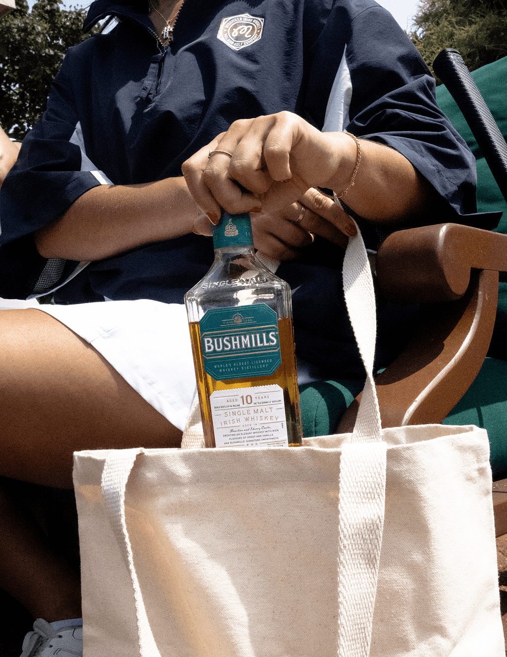Bushmills 10 Year Single Malt Whiskey being being pulled out of the Bushmills x Malbon tote bag.