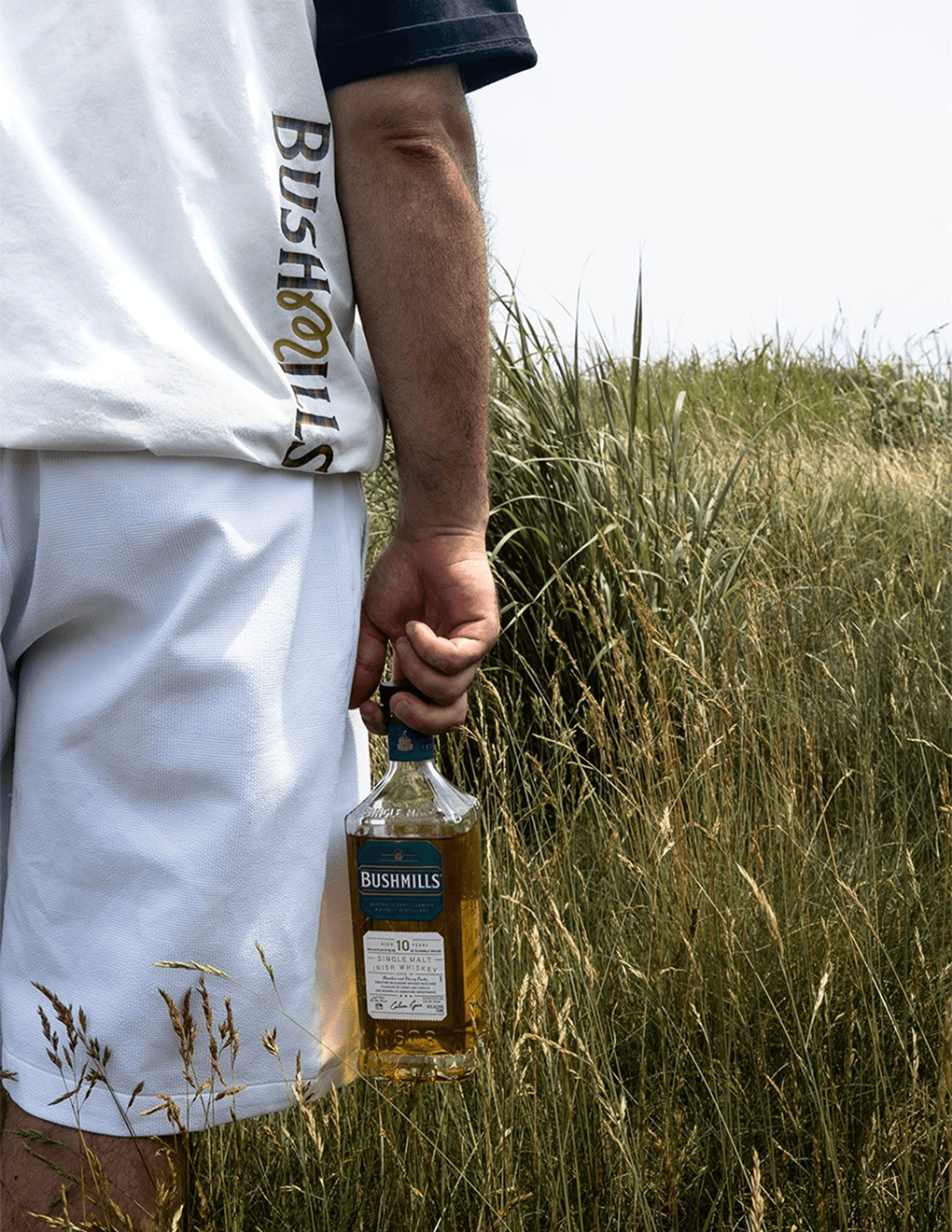 Detail shot of Bushmills x Malbon collab logo on Bushmills x Malbon white vest, modeled on a man on a golf course holding Bushmills 10 Year Single Malt.