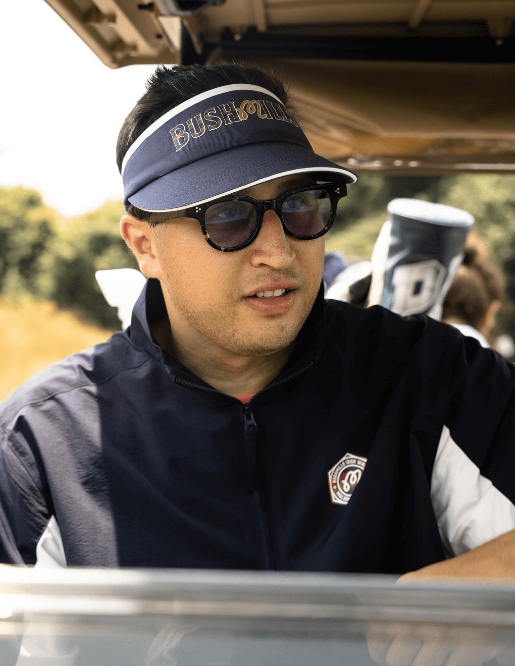 Man wearing Bushmills x Malbon navy visor in a golf cart on golf course.