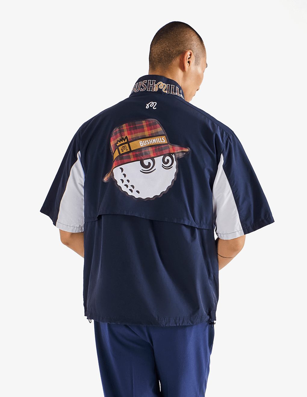 Male modeling back of Bushmills x Malbon navy windshirt with large Buckets cartoon logo.