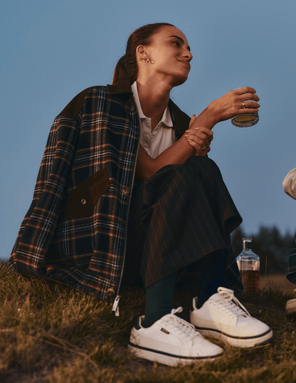 Bushmills X Malbon Wool & Leather Jacket on a female model on the golf course with a cocktail in hand.