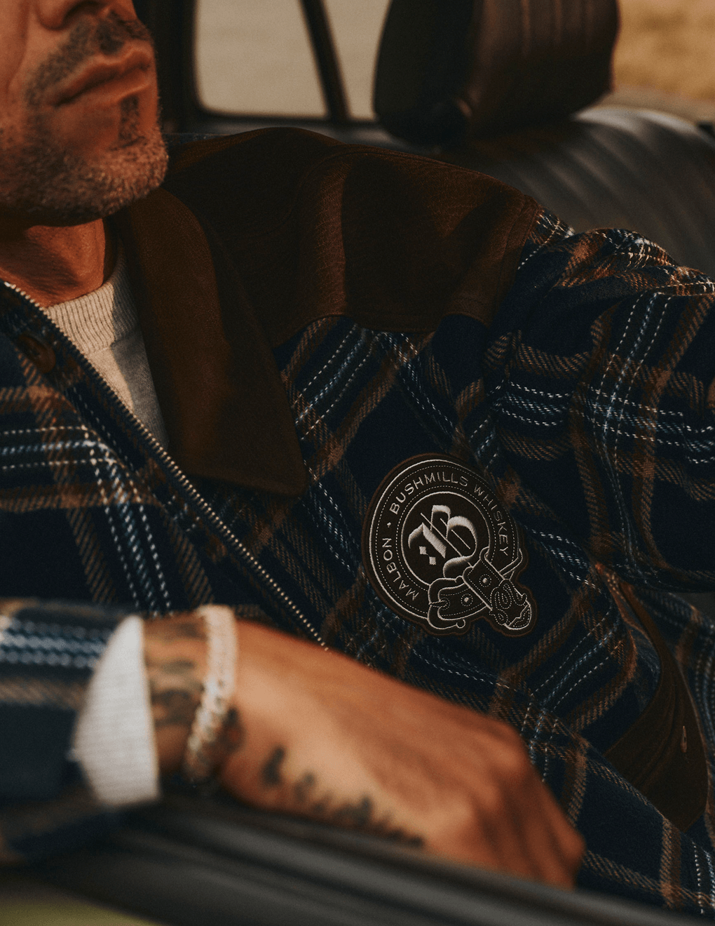 Close up of Bushmills X Malbon Wool & Leather Jacket on a model in a car on the golf course.