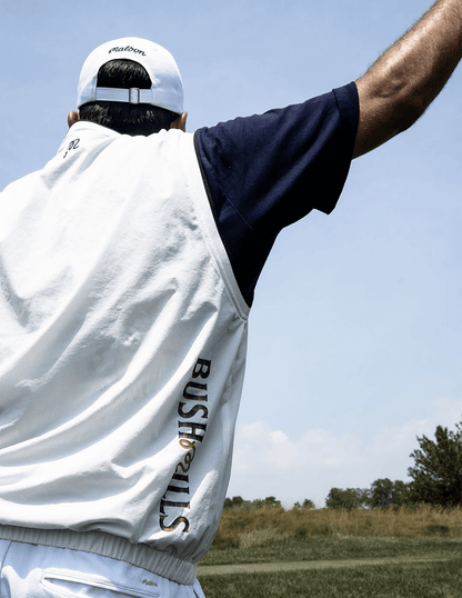 Detail shot of Bushmills x Malbon collab logo on Bushmills x Malbon white vest, modeled on a man on a golf course.